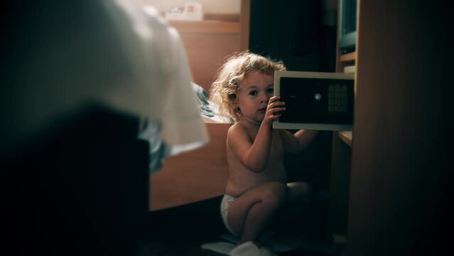 Funny little kid looks into a safe box in the hotel room