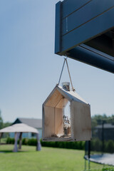 Modern bird house (with bird feeder in middle) made of light wood hanged on side of garage in domestic area