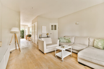 a living room with wood flooring and white furniture in the center of the room is an open kitchen area