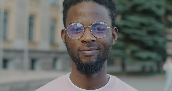 Slow motion portrait of cheerful African American man looking at camera with smile standing outside alone. Positive emotion and urban life concept.