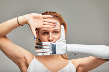 Studio portrait of a young girl with disability wearing sensory bionic prosthetic arm. Beautiful woman folded her hands in a frame in front of her face fully controlling her artificial robotic hand.