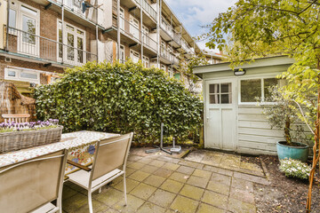 a patio with chairs and table in the middle of an apartment complex, surrounded by trees and plants on a sunny day