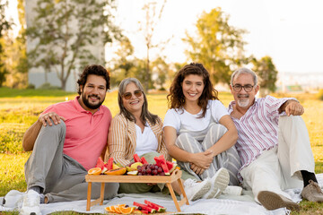 Glad european old and adult family enjoy picnic, talk, fruits and eat food