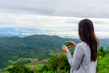 Woman drinks morning coffee or tea outdoor enjoying green mountain view background, during vacation on the mountain, holiday concept.