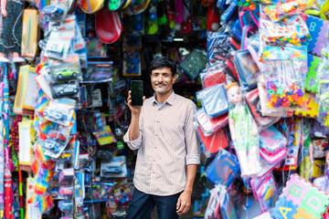Indian roadside toy shop vendor, seller standing in front with currency or smartphone