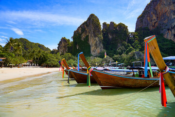 Naklejka na ściany i meble Traditional Thai longtail boats beached on the golden sand of Railay West Beach in front of rocky karst outcrops in the Province of Krabi, Thailand, Southeast Asia