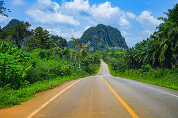 Winding road passing through a lush jungle surrounded by limestone karst cliffs in southeast Asia...