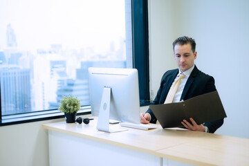 Business person looking at hard copy file with intense and serious emotion at desk beside window with hugh building view in office room in capital city. - obrazy, fototapety, plakaty
