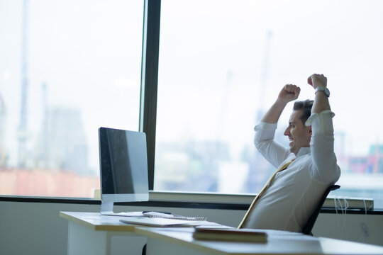 Business man fist his hands over head, success emotion of employer sitting in front of destop at desk with smile of happiness.