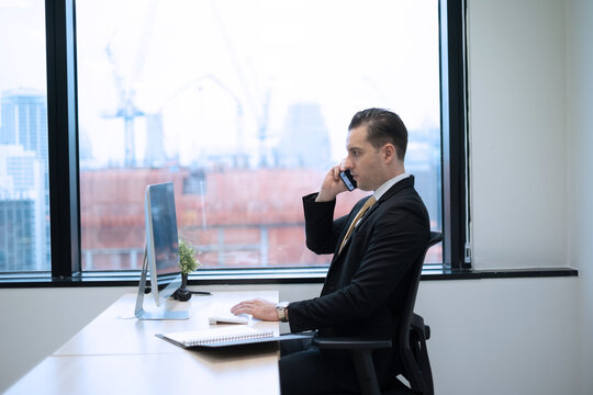 Business man using smartphone contact customer at desk on office in city with high building view, serious and intense emotion business onwer sitting beside glass window.