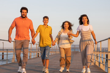 Glad european teen and millennial people holding hands, enjoying vacation on beach, walk outdoor