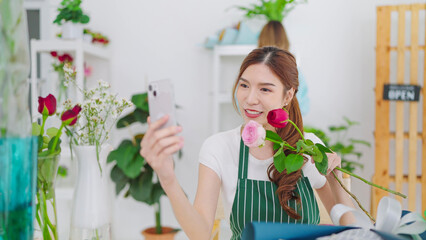 Young asian women owner floral store holding rose flowers on hands showing to client choosing through video call on smartphone for taking order. Small business concept