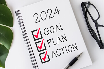2024 Goal, Plan, Action checklist text on note pad with glasses and pen.