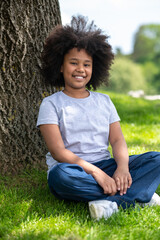 Little girl sitting on grass under tree resting in nature enjoying freshair.