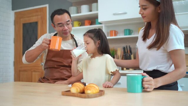 Happy Asian family with father,  mother, and little girl enjoy cooking and having a breakfast together, parent making a vegetable salad in a bowl with daughter.