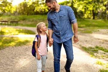 First day at school. Happy father leading his little child school girl in first grade, holding hands with daughter