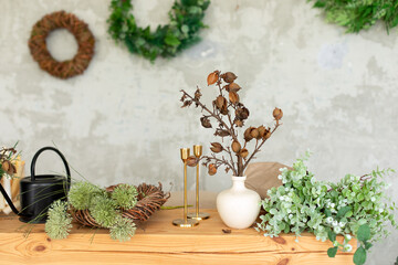 Wooden table on which there are watering can, wreath, green plants, gardening tools, dried flowers...