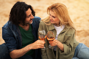Romantic young couple toasting each other with wine while sitting on beach
