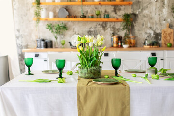 Table festive setting with tulips flowers and stabilization moss in glass vase. Wedding table decoration. Beautiful served table with runner on table, wineglass and plates in living room	