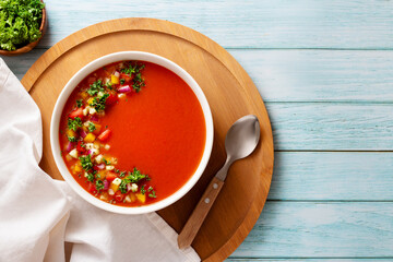 Spanish tomato gazpacho cold soup styled and decorated in white plate with ingredients on wooden plank table, top view