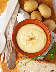 Top view of a plate of sauce with ingredients: parsley, potatoes, cheese, saffron, cheese, garlic and bread