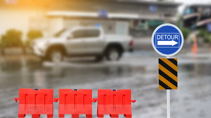 Blue traffic sign with graphic of right detour directional arrow due to flood and red road barriers...
