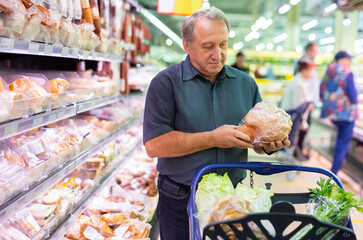 Elderly man chooses chicken meat in supermarket