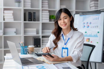 Portrait of a smiling asian businesswoman using mobile phone in the office. Young Asian businesswoman with paperwork at workplace using smartphone in a modern office.