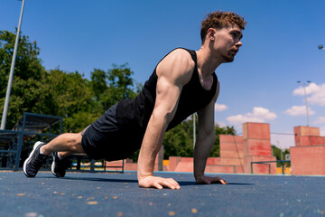 young pumped-up athlete doing push-ups from the ground during street training endurance exercise...