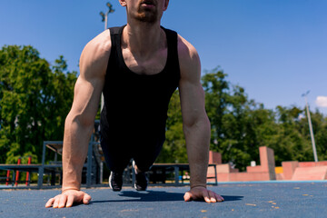 Fototapeta premium young pumped-up athlete doing push-ups from the ground during street training endurance exercise swings arms and shoulders