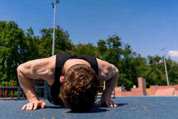 young pumped-up athlete doing push-ups from the ground during street training endurance exercise...