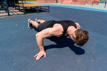 Fototapeta na wymiar young pumped-up athlete doing push-ups from the ground during street training endurance exercise swings arms and shoulders