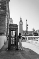 Fototapeta na wymiar Girl leaning against a telephone booth in London, with the tower of Big Ben in the background. Black and white photo.