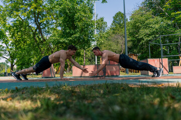trainer and young sportsman doing push-ups on the street and giving each other a high five during...