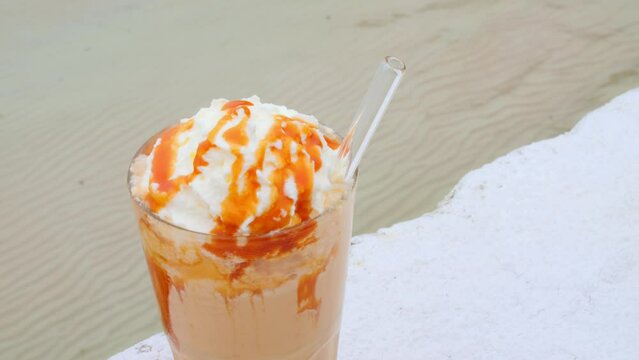 Chocolate cocktail with caramel and transparent eco straw. Delicious chocolate cocktail and caramel on the top near ocean waves freshness. Enjoy fragrant cold chocolate cocktail in hot summer day.