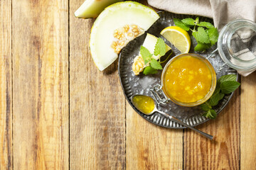 Fototapeta na wymiar Sweet melon and citrus jam or jelly in small glass jar with fresh melon slices on wooden rustic table. Homemade preserve. View from above. Copy space.
