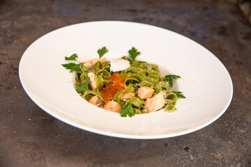 green pasta with salmon and red caviar and greens in a white plate