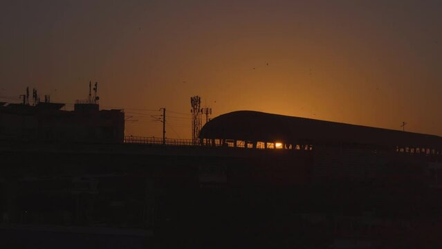 panning orange dusk shot with silhouette of buildings, metro station with kites flying in the sky on the traditional festival of sankranti uttarayan independence day in India