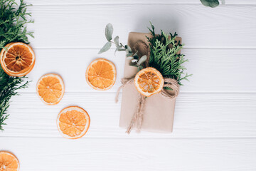 The gift is wrapped in brown paper and tied with twine with thuja and eucalyptus on a white wooden background. Top view