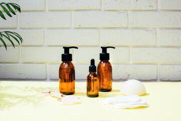 Amber bottles with facial treatment on a yellow table with green leaves on backdrop. Front view