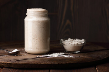 Sourdough bread starter with bubbles with white flour on dark wooden rustic background, fermentation, natural homemade baking and cuisine concept
