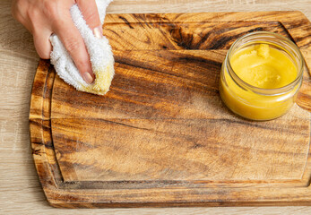 Woman hands apply homemade beeswax wood treatment polish to restore natural wood cutting board....