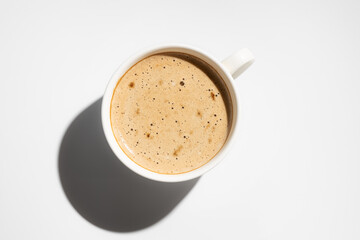 Cup of cappuccino with creamy foam on white background. Copy space. Hard light, top view