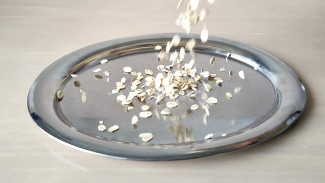 Haferflocken fallen in Zeitlupe auf silbernen Teller, Fr&uuml;hst&uuml;ck, Cerealien, langsam, aussch&uuml;tten, viele, gr&uuml;n, 4k, Bio