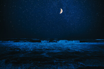 Crescent moon in starry sky over sea at night