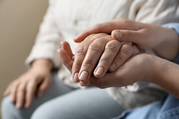 Woman holding hands with her mother on beige background, closeup. Space for text