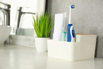 Electric toothbrushes and tube of paste on white countertop in bathroom. Space for text