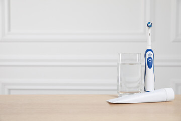 Electric toothbrush, glass of water and toothpaste on wooden table. Space for text