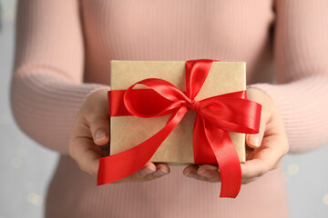 Woman holding gift box with red bow on light grey background, closeup