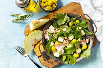 Summer mediterranean salad with melon, bacon, olives, white cheese and arugula on blue stone...